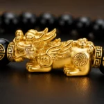 Close-up of black obsidian bracelet with ornate gold-tone Pixiu charm and feng shui symbols