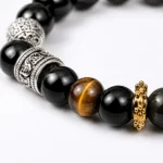 Close-up of black obsidian and tiger eye bracelet with engraved silver-tone and gold-tone spacer details