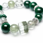 Close-up detail of an emerald green mixed crystal bracelet with malachite style beads, green rutilated crystal bead, and transparent cube crystal centerpiece