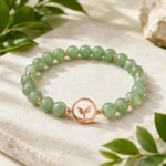 Green aventurine growth and renewal bracelet with rose gold leaf charm on natural stone background