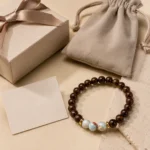 Natural dark wood and blue gemstone bracelet displayed with a beige gift box, velvet pouch and message card