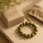 Olive green wood bead bracelet displayed beside a jewelry box and soft drawstring pouch