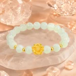 Pale green gemstone lotus bracelet with gold-tone flower centerpiece displayed among clear crystals