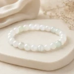 Pale green and white stone bead bracelet displayed on a warm ivory jewelry stand