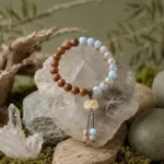 Blue gemstone and natural wood bead bracelet with lotus tassel charm displayed on clear quartz crystal