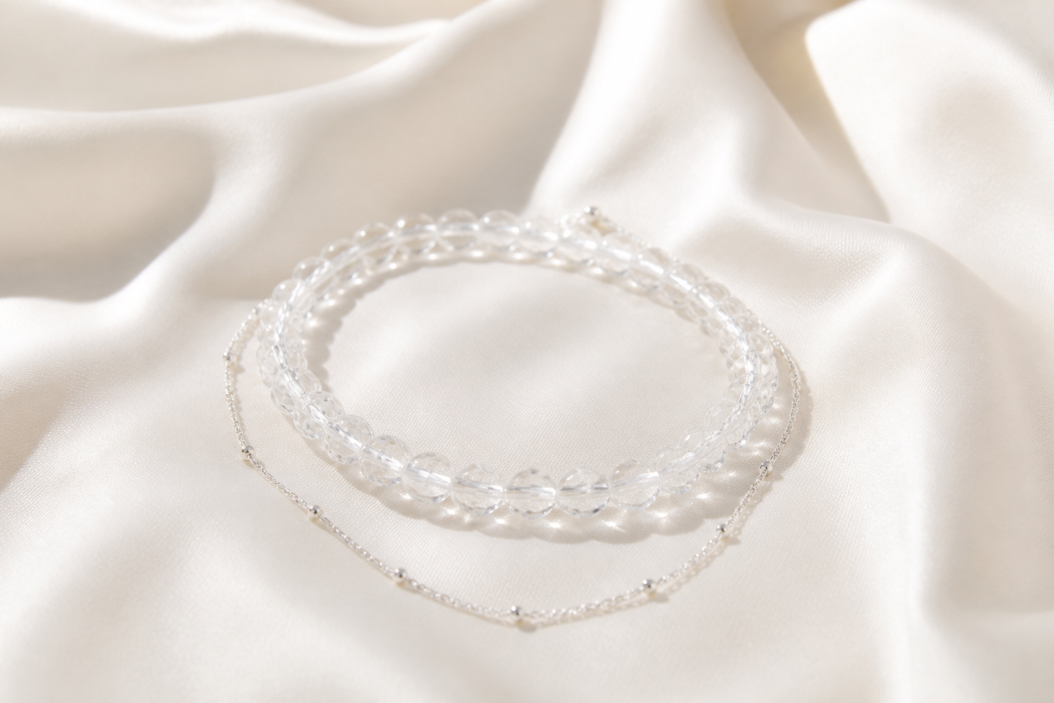 Clear quartz bead bracelet layered with a silver chain on ivory silk
