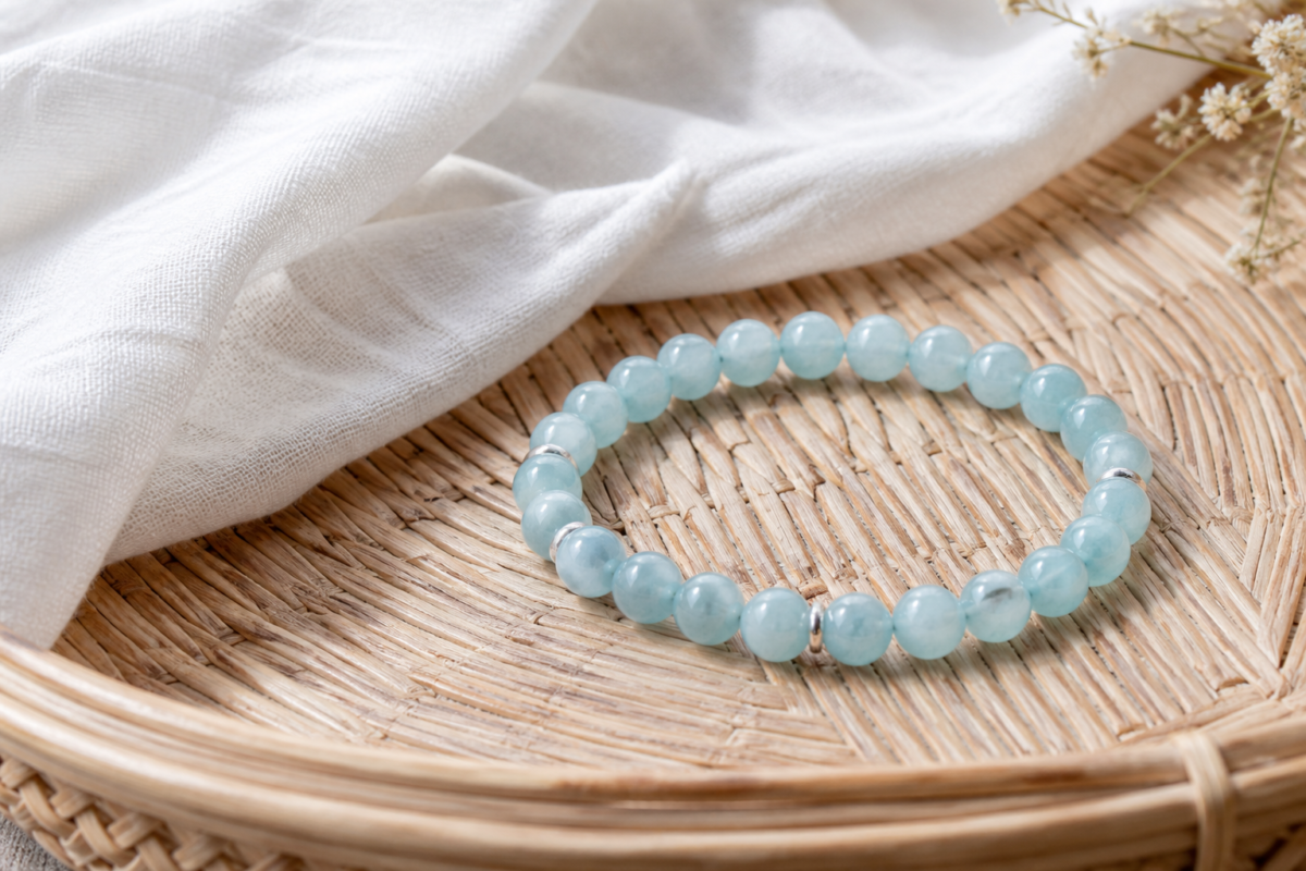 Aquamarine bead bracelet on a rattan tray with airy white cotton fabric