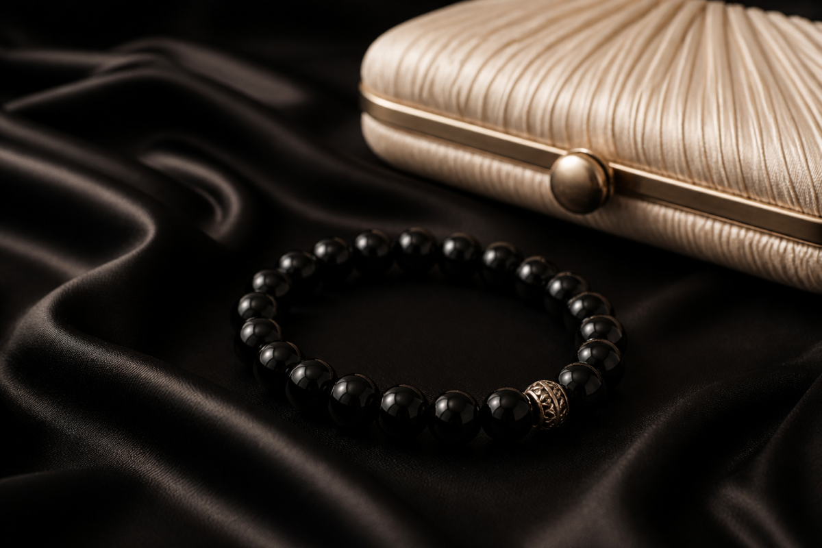 Black onyx bead bracelet on black satin beside a cream evening clutch