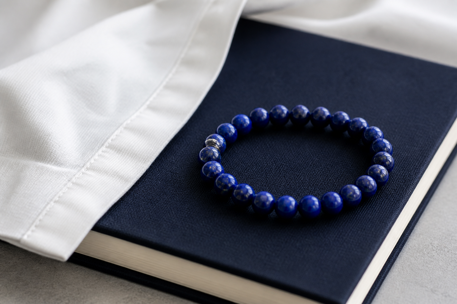 Deep blue lapis lazuli bead bracelet beside navy fabric and white shirt cloth