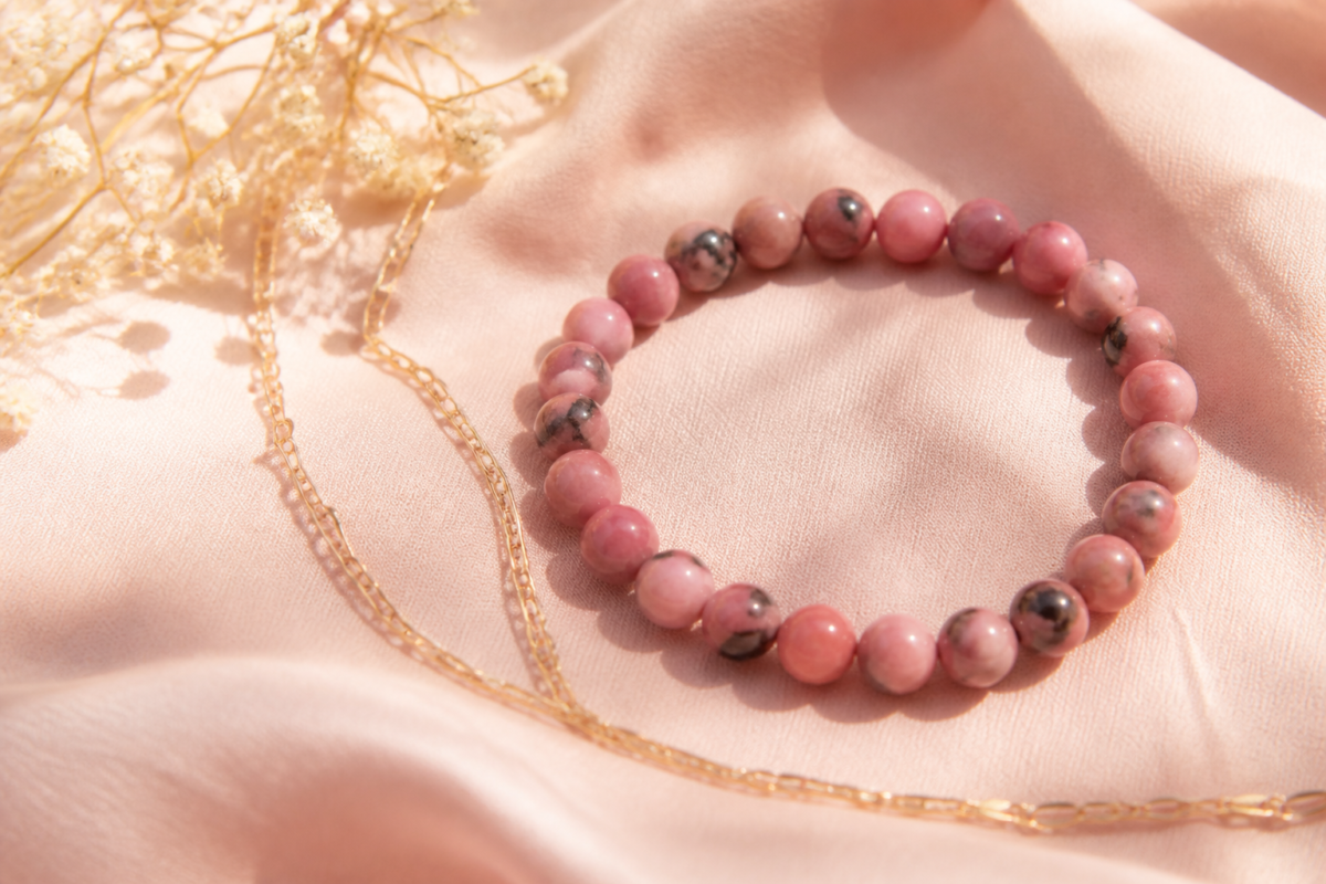 Rose pink rhodonite bead bracelet on blush cotton beside a gold tone chain