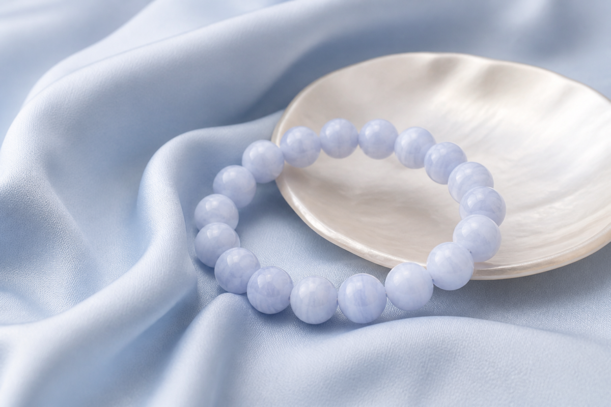 Blue lace agate bead bracelet on powder blue silk beside a pearl toned dish