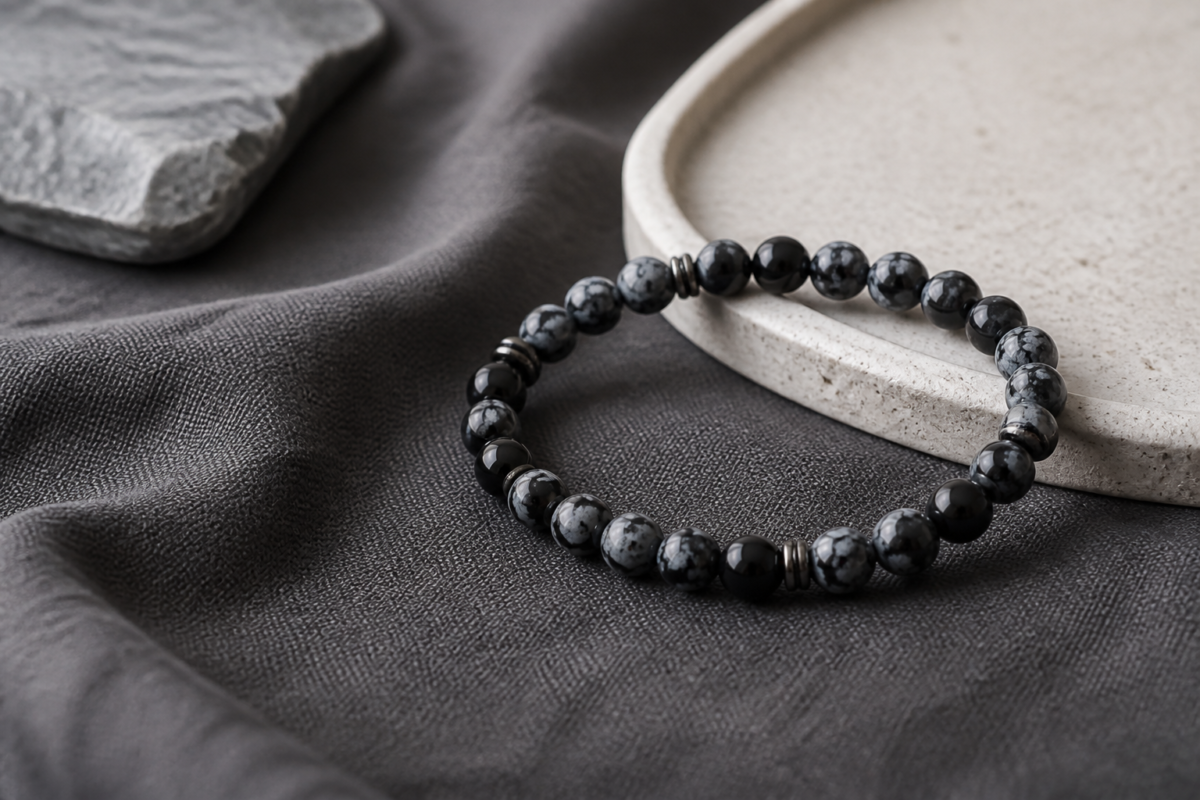 Snowflake obsidian bead bracelet on charcoal linen with a pale stone tray