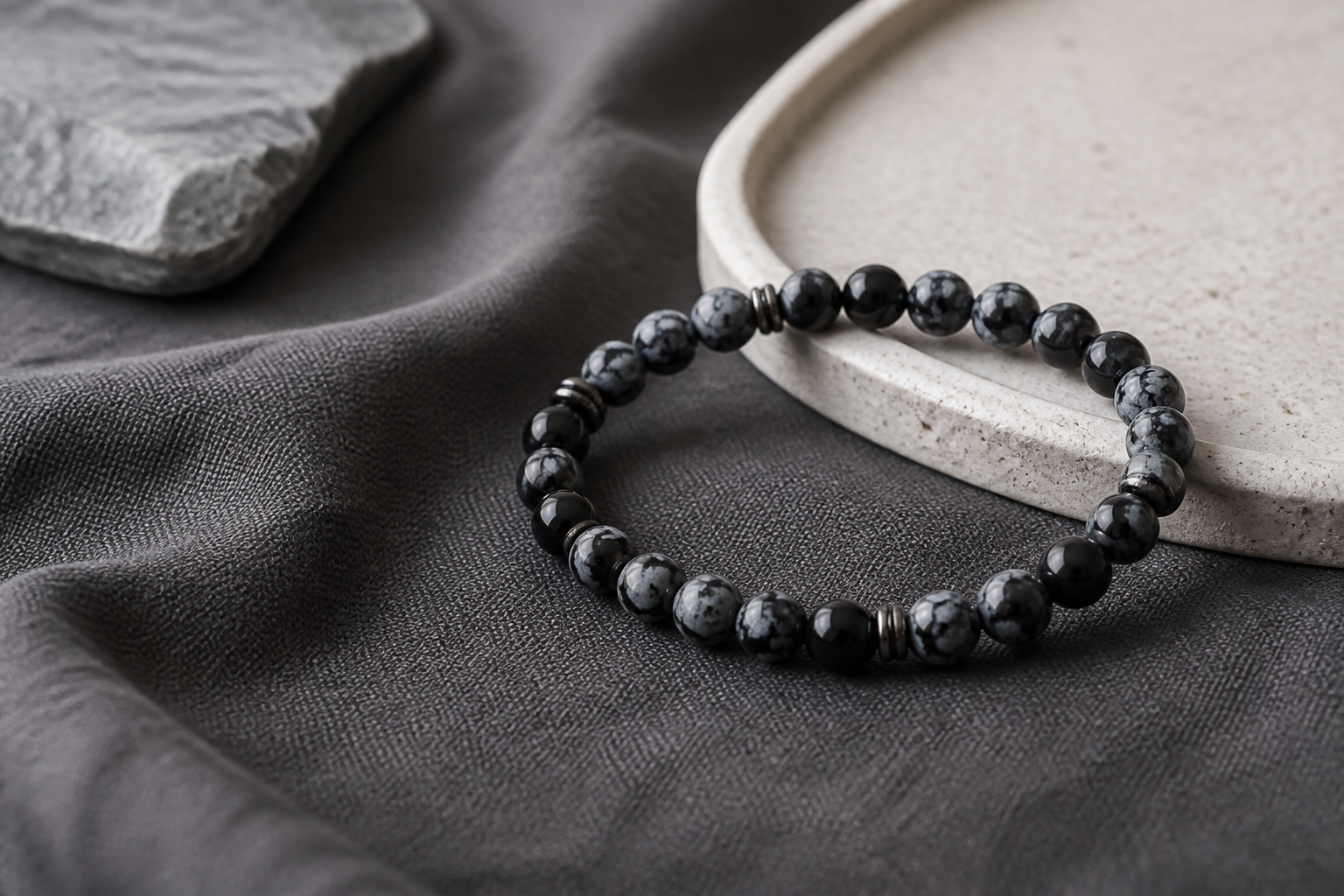 Snowflake obsidian bead bracelet on charcoal linen with a pale stone tray