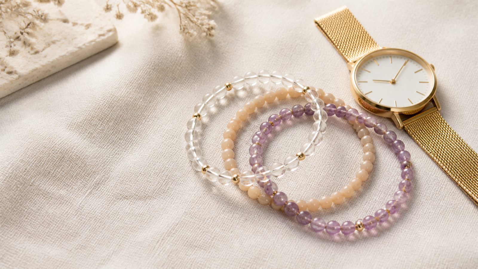 Three crystal bead bracelets layered beside a gold watch on pale linen