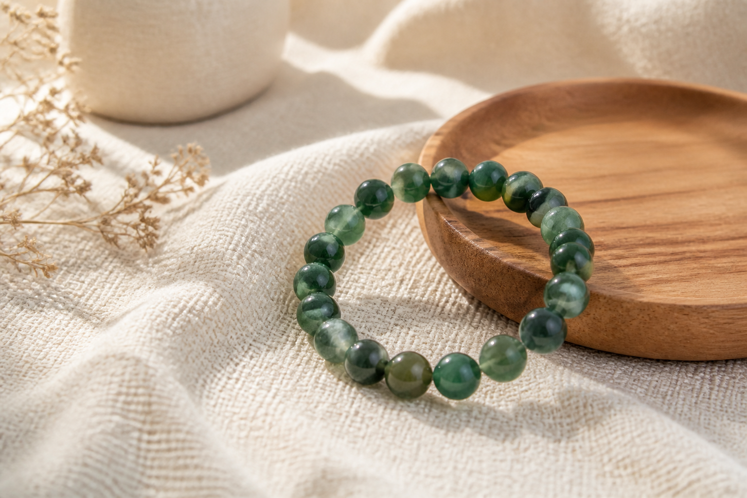 Green agate bead bracelet on cream woven fabric and wood dish