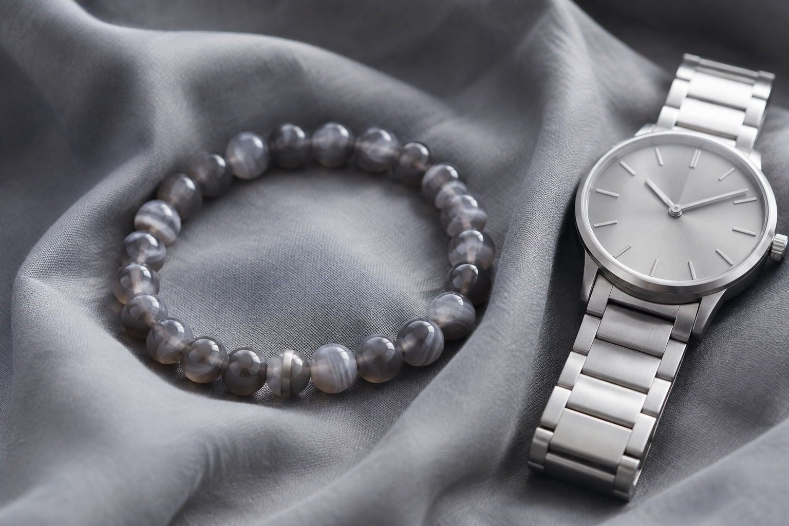 Grey agate bead bracelet on smoky grey cotton beside a brushed silver watch