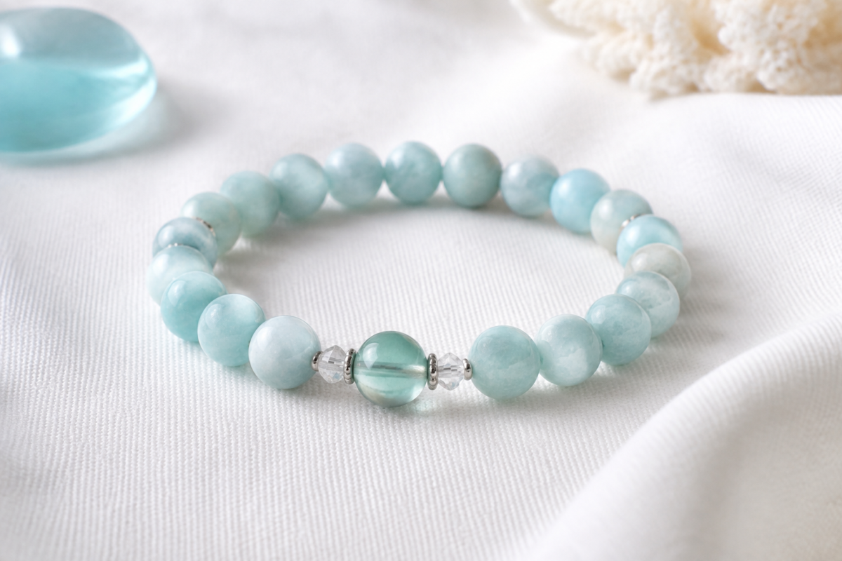 Amazonite pale aqua bead bracelet on white woven fabric beside a soft blue glass accent