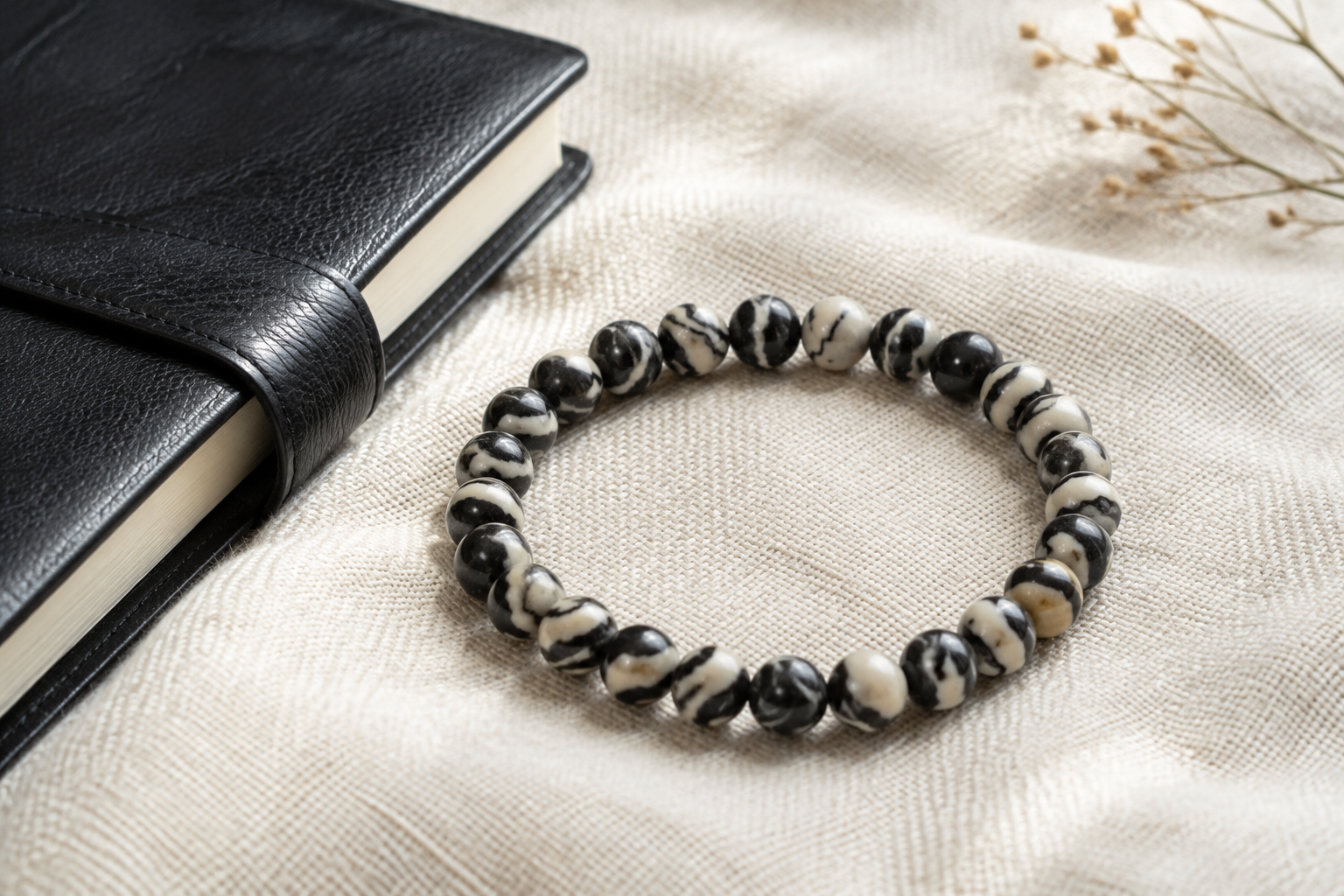 Zebra jasper black and cream striped bead bracelet on oat fabric beside a black notebook