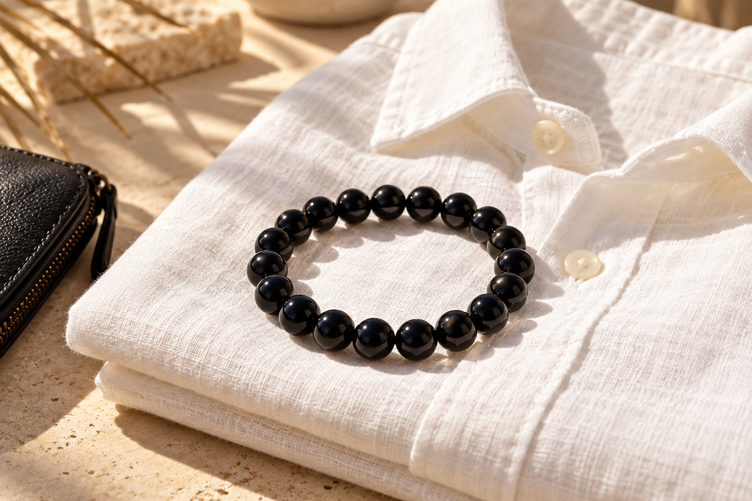 Glossy black bead bracelet on a folded white linen shirt with a dark accessory nearby