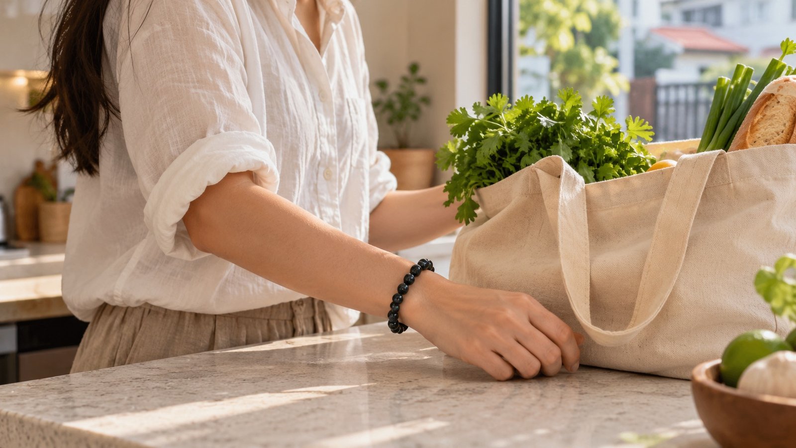 Dark gemstone bracelet on a wrist beside a reusable canvas grocery bag filled with herbs on a kitchen counter