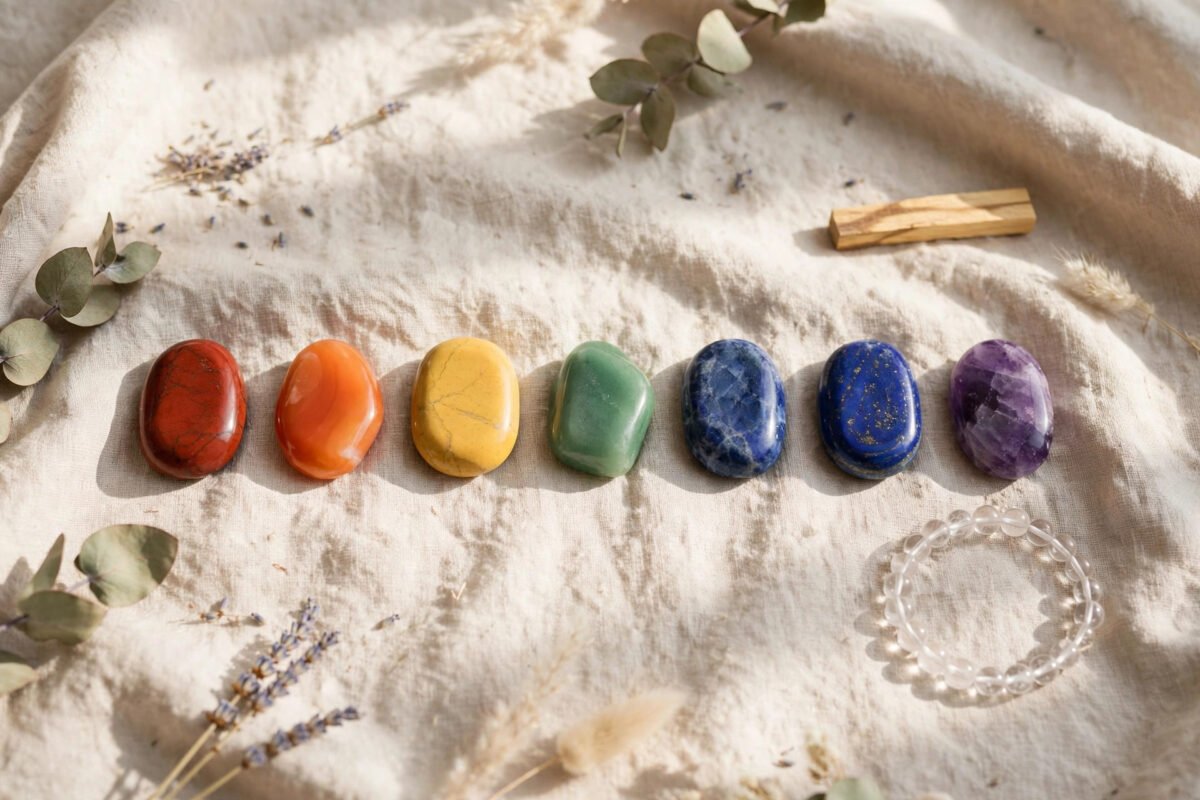 Flat lay of seven chakra stones in a line on a soft blanket with a crystal bracelet nearby