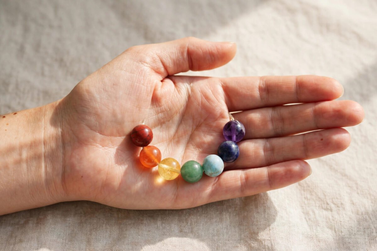 Seven chakra crystal bracelet held in open hands over a calm neutral background in daylight